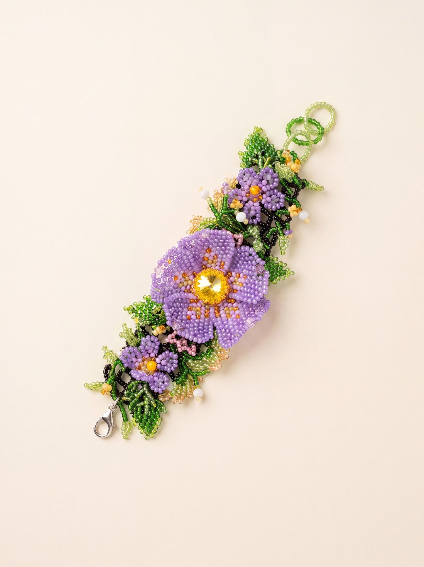 Handmade beaded flower bracelet "Violets" with purple seed-bead flowers and green leaves, curved on a cream background