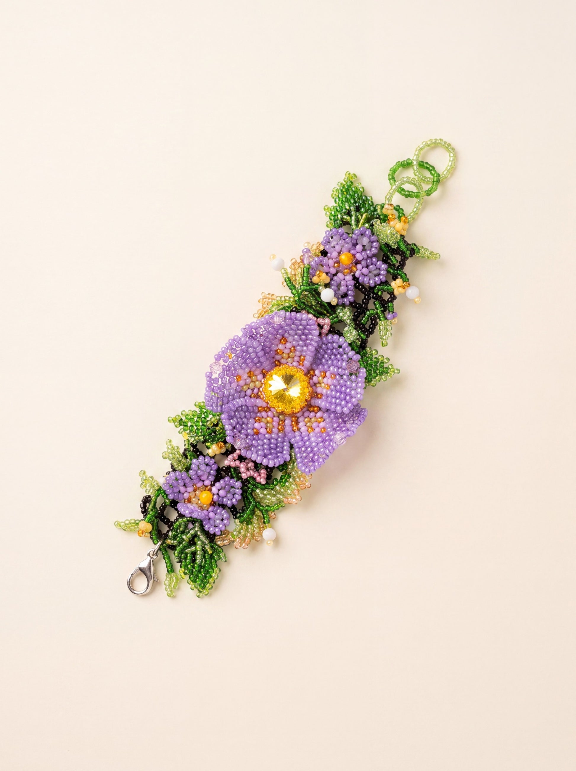 Handmade beaded flower bracelet "Violets" with purple seed-bead flowers and green leaves, curved on a cream background