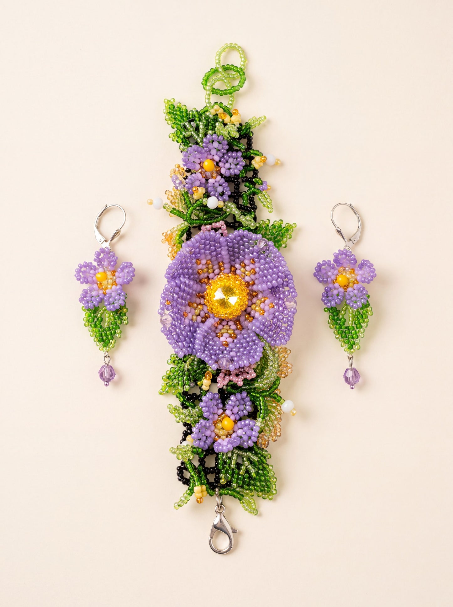 "Violets" bracelet laid vertically with one beaded earring on each side of the large flower