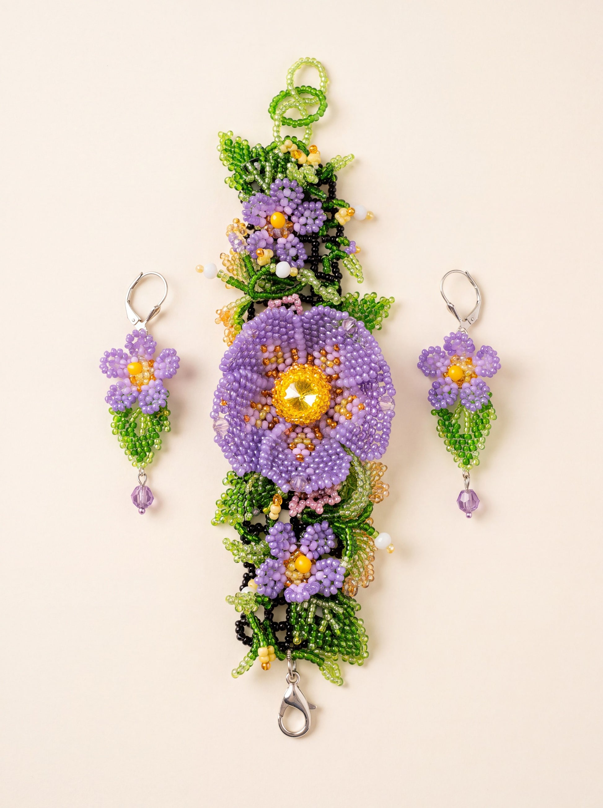 "Violets" bracelet laid vertically with one beaded earring on each side of the large flower