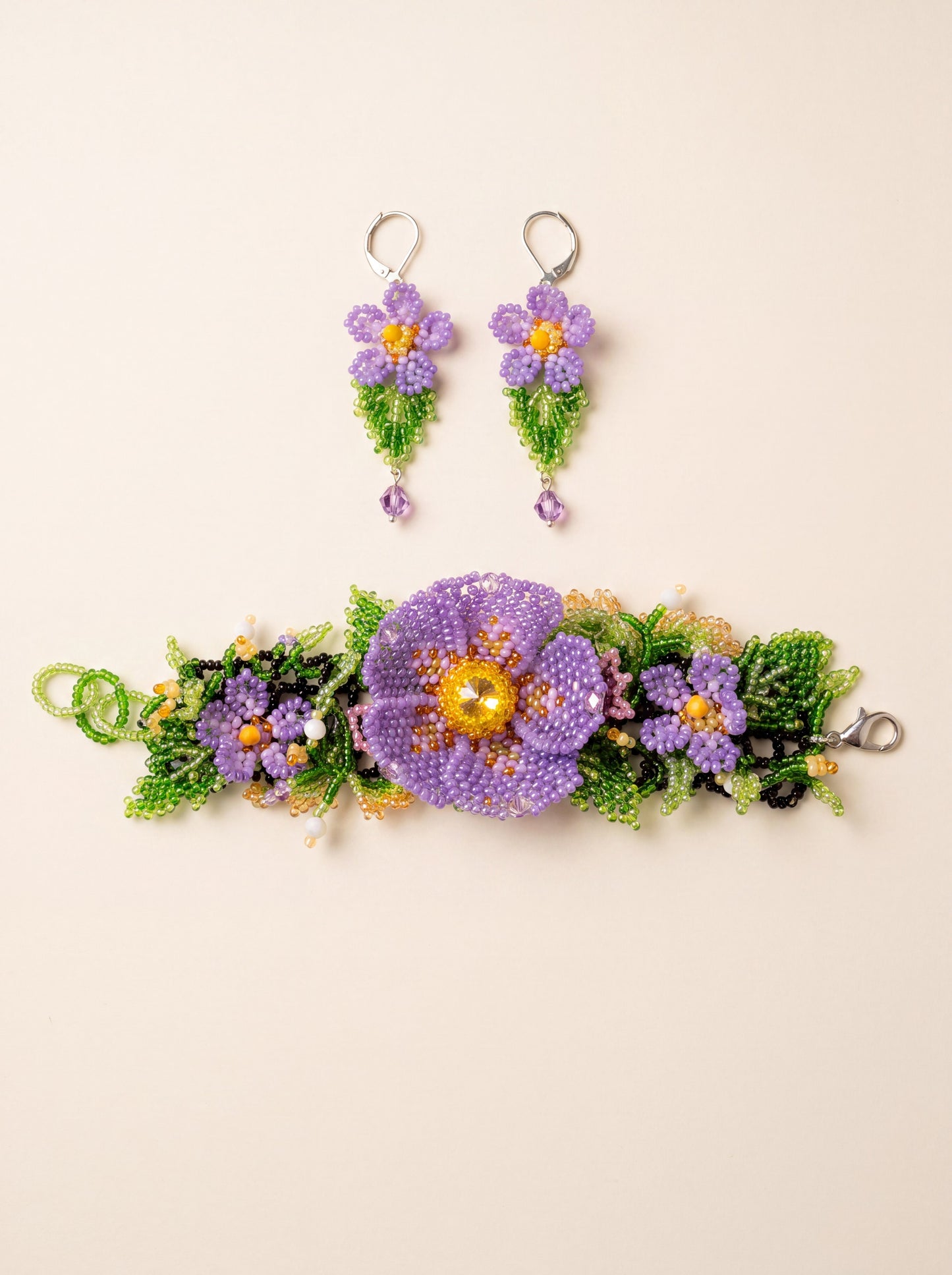 Handmade beaded set "Violets" — bracelet with three purple seed-bead flowers on a black net band and matching drop earrings, on cream
