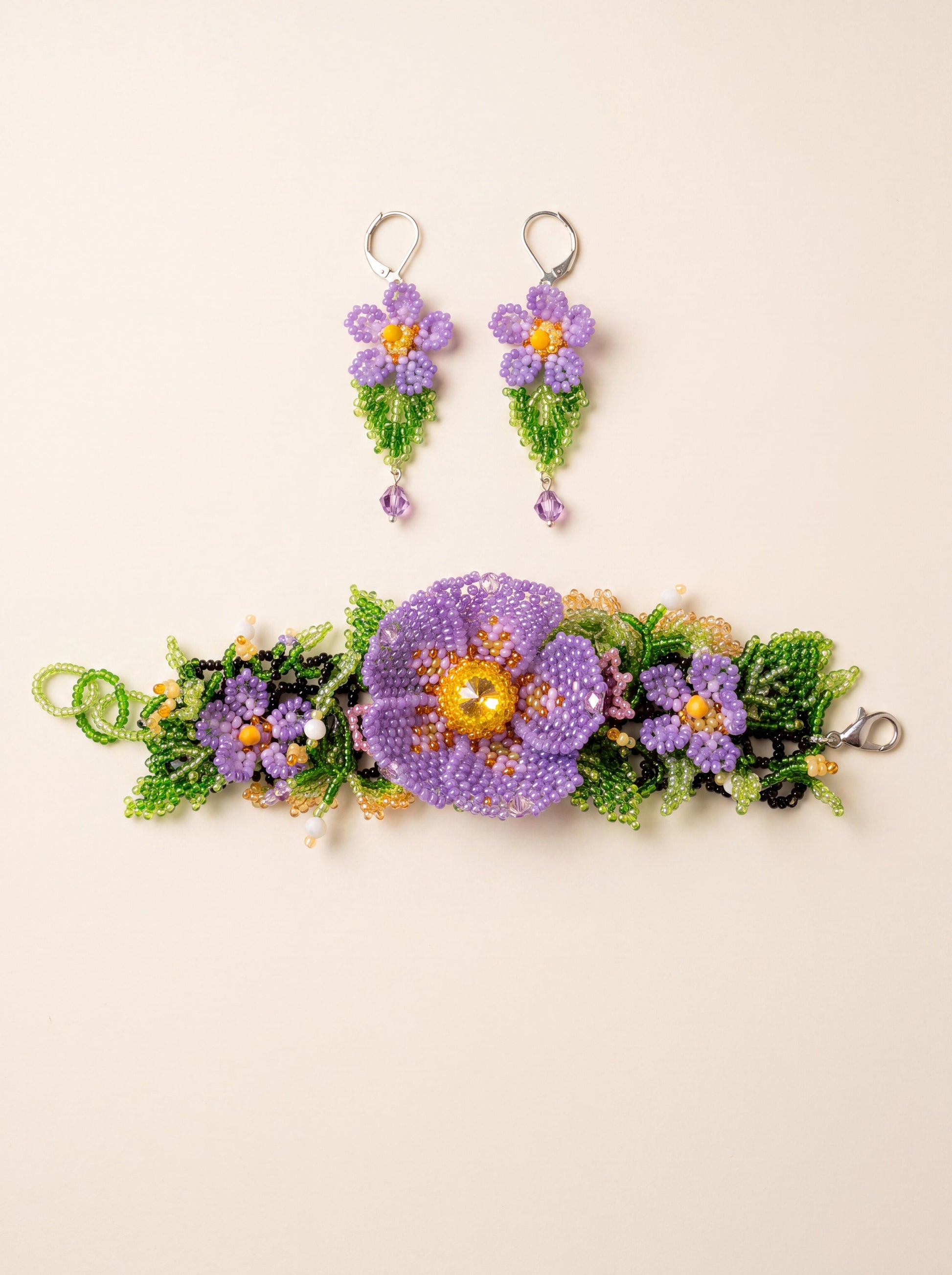 Handmade beaded set "Violets" — bracelet with three purple seed-bead flowers on a black net band and matching drop earrings, on cream