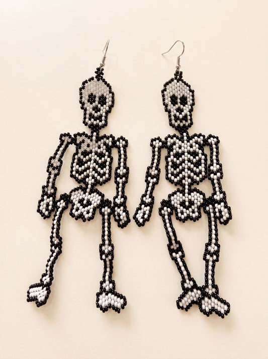 Handmade beaded skeleton earrings, articulated black and white seed-bead skeletons on silver hooks, on cream