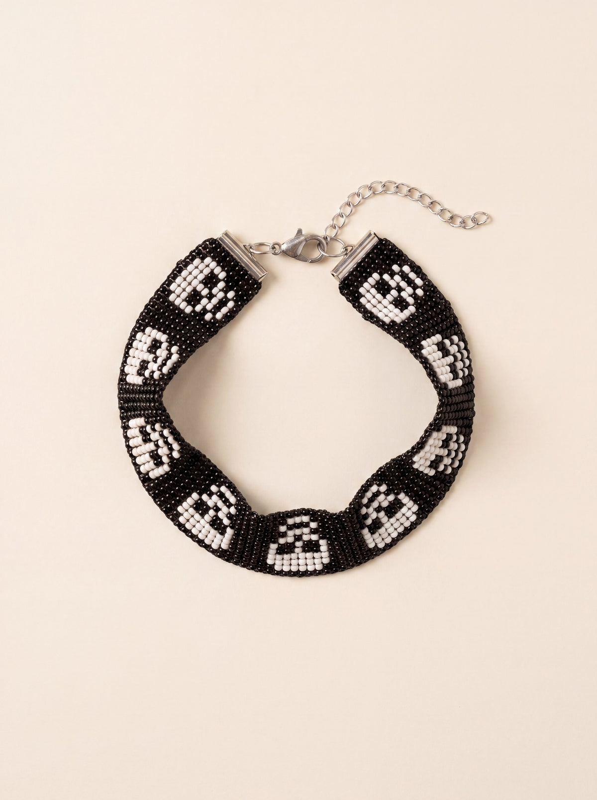 Handmade loom-beaded black bracelet with a row of white skulls, coiled flat on cream