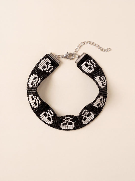 Handmade loom-beaded black bracelet with a row of white skulls, coiled flat on cream
