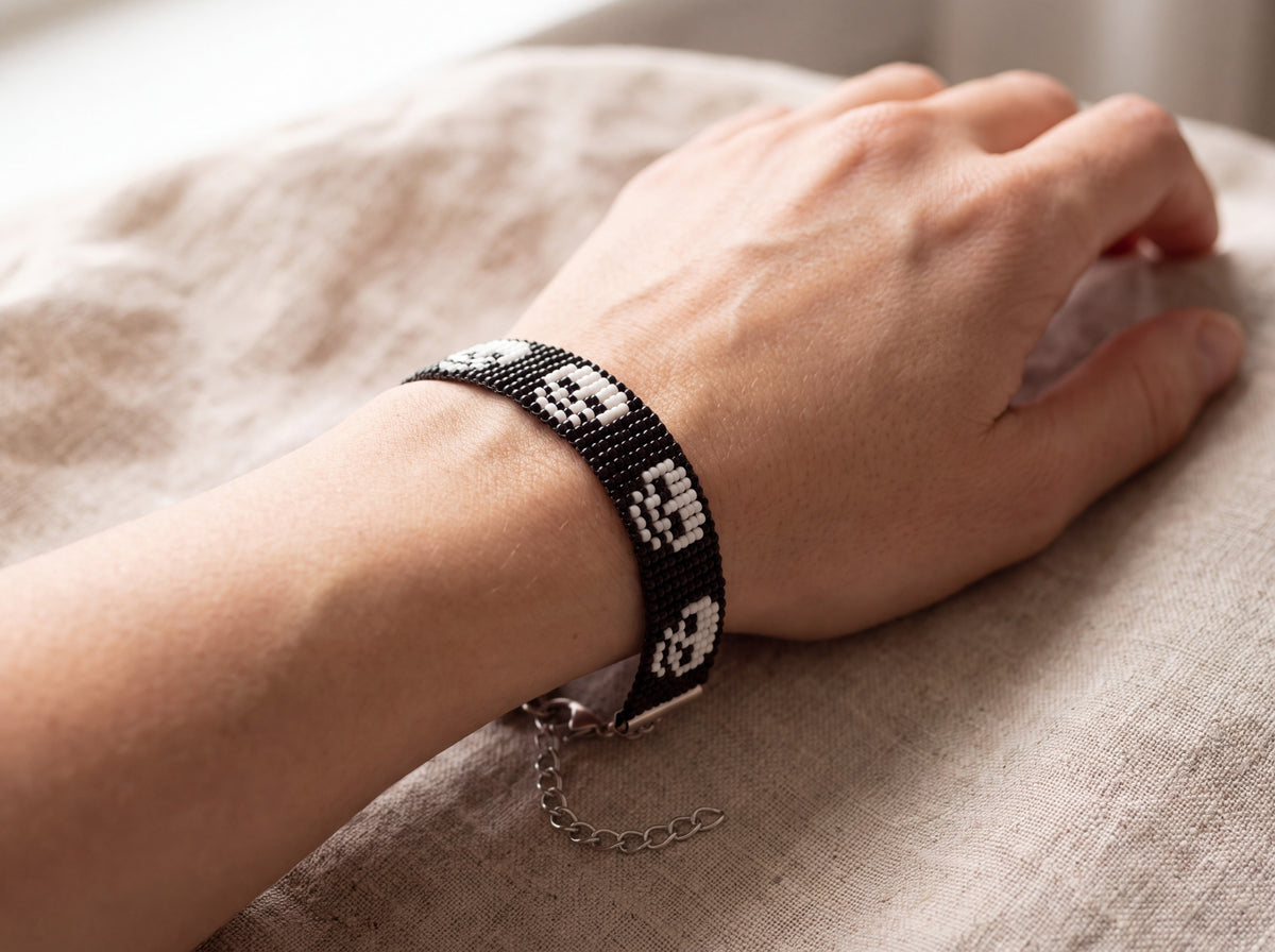 Black beaded skull bracelet worn on the wrist with a relaxed hand on linen
