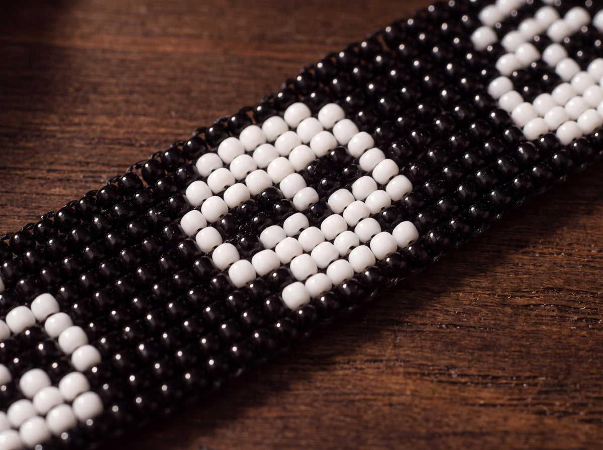 Macro detail of one white beaded skull on the black loomed band, on dark wood