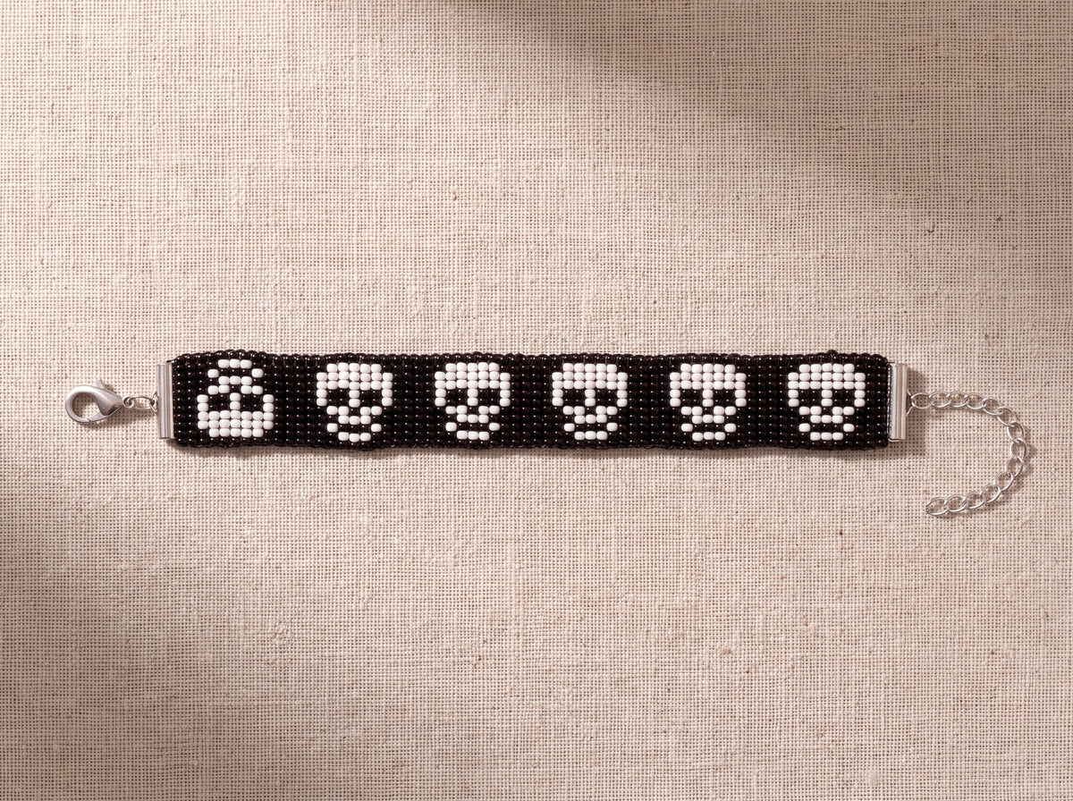 Skull loom bracelet laid out full length showing clasp and extension chain, on oatmeal linen