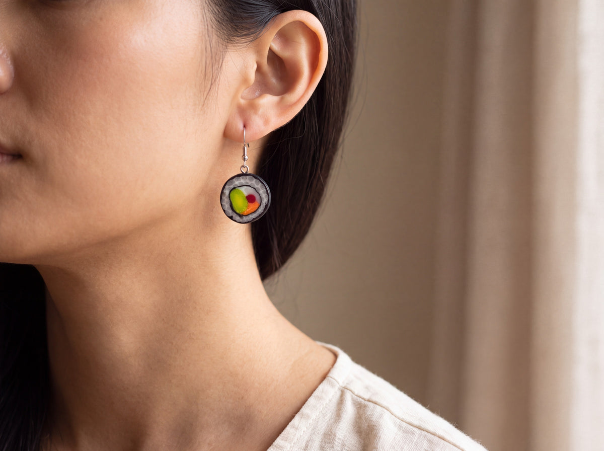 Handmade polymer clay sushi roll earring with avocado, salmon and tuna detail on a silver hook, shown worn on a model's ear