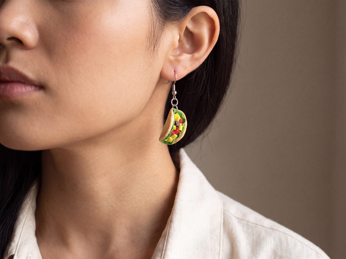 Handmade miniature taco earring with lettuce, cheese, and salsa detail on a silver hook, worn on a model's ear.