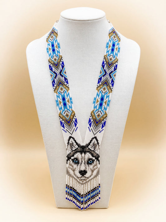 Handmade beaded wolf necklace with a geometric wolf face motif in blue, gold, white and black seed beads, fringed ends.
