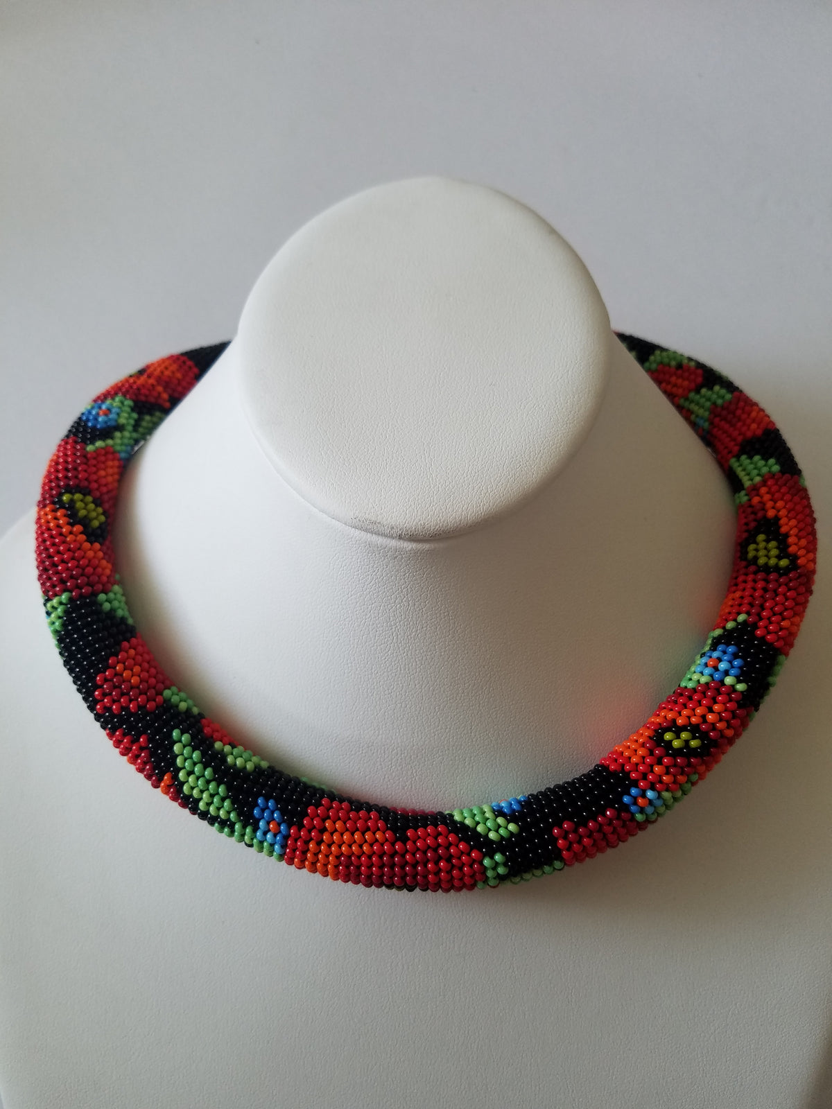 Handmade poppy beadwork choker in black and red displayed on a white leather necklace bust