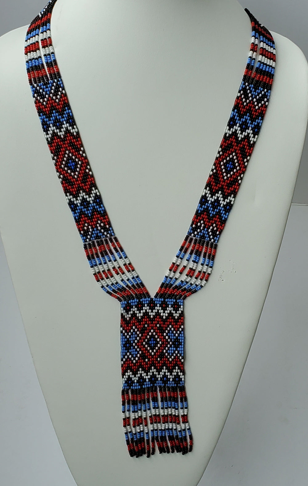 Glass seed bead gerdan necklace in red, blue, white and black diamond pattern displayed on a white bust