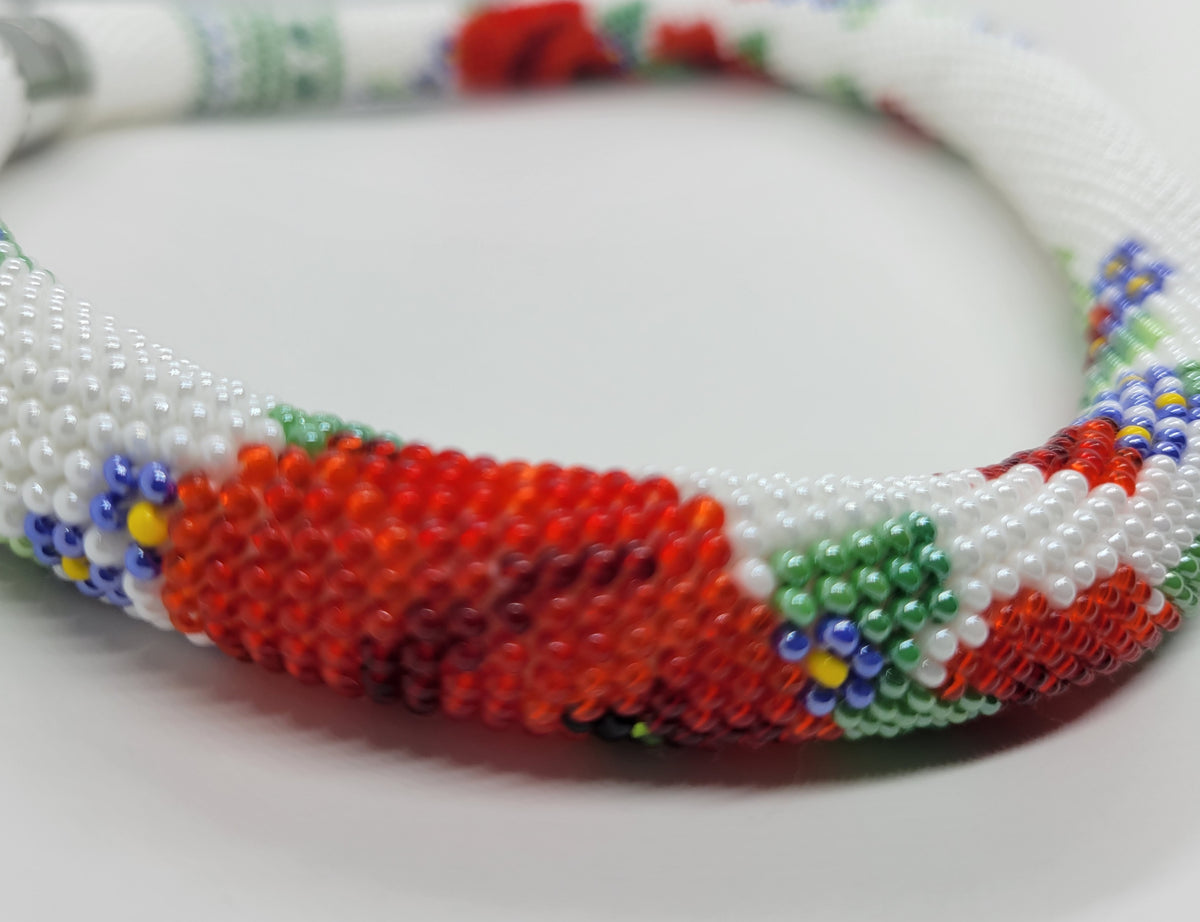 Soft-focus close-up of red poppy and blue flower beadwork on the handmade Poppies choker