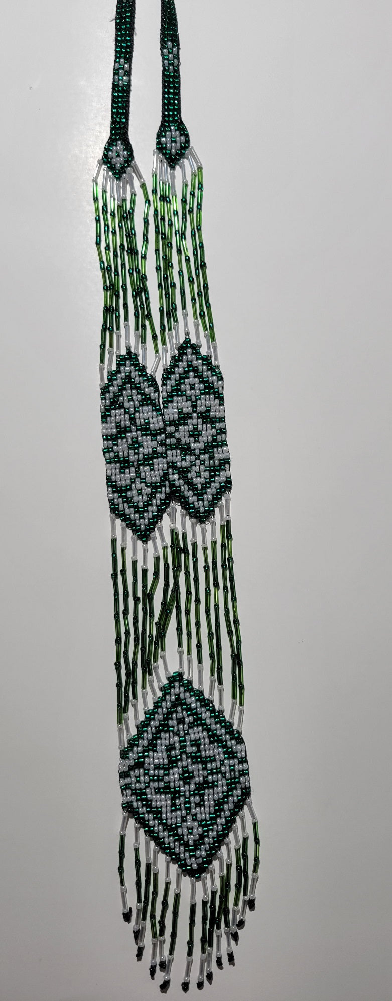 Dark green and pearl white loomed gerdan necklace hanging to show its beaded fringe