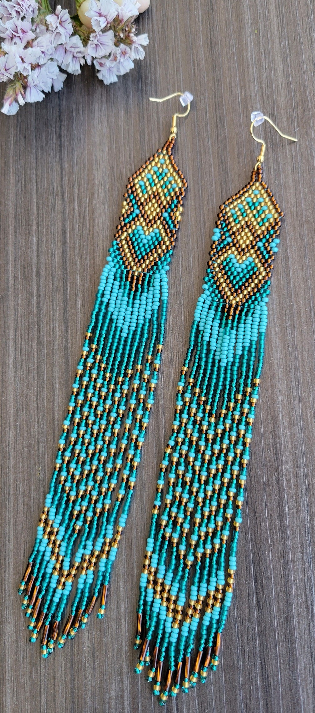 Extra long fringe earrings beaded in teal and gold with a heart pattern, styled with white cherry blossoms
