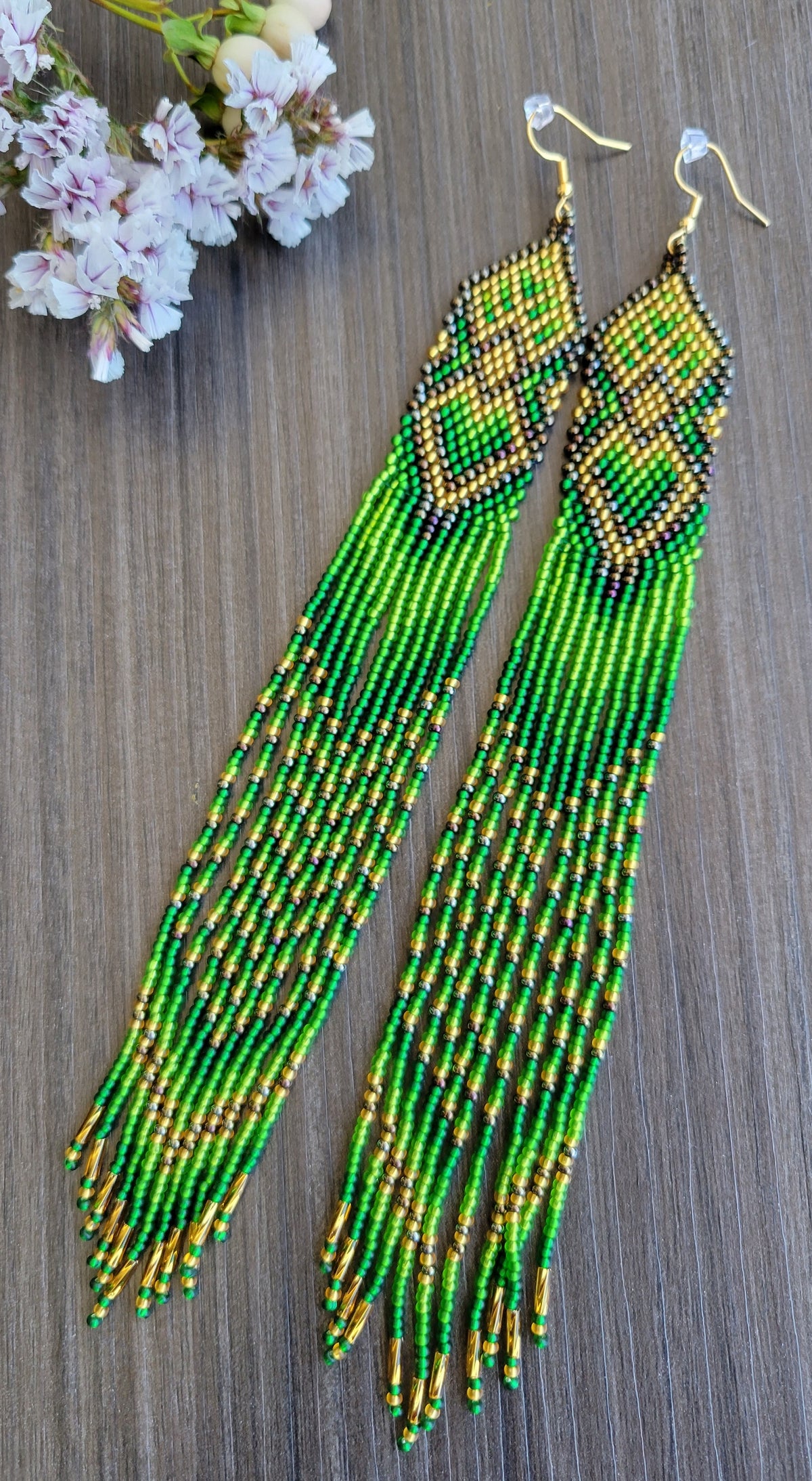 Green and gold extra long beaded tassel earrings, handmade with glass seed beads, shown on rustic wood