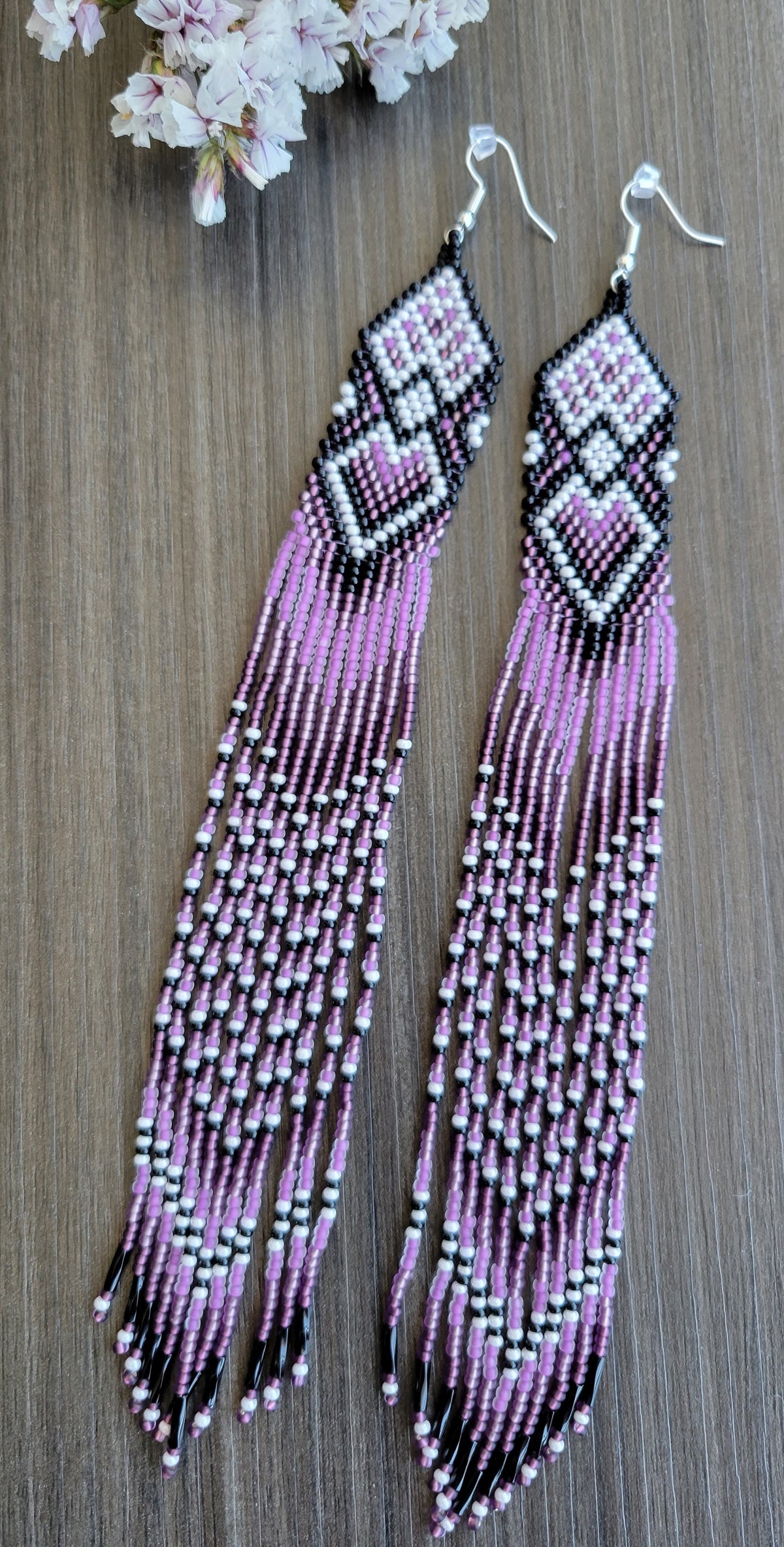 Extra long beaded earrings in purple and lilac with white heart accents, flat lay with spring flowers