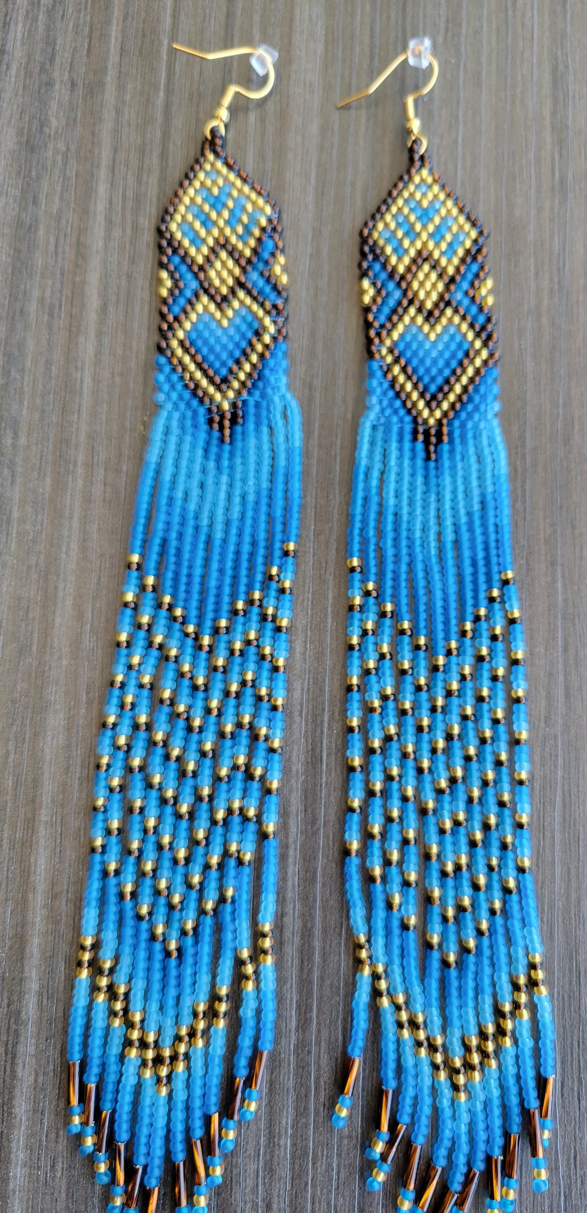 Handmade extra long seed bead earrings in blue and gold with heart motif, photographed on weathered wood
