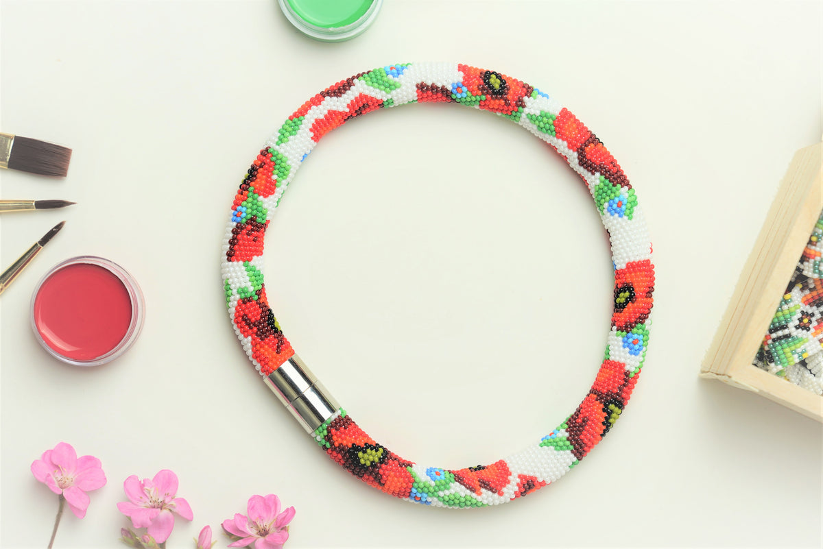 Flat lay of the Poppies beaded choker with silver magnetic clasp among paints, brushes and pink flowers