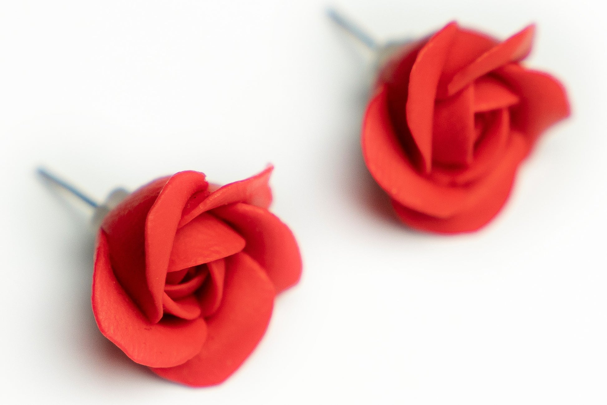 Close-up of red polymer clay rose stud earrings showing hand-formed petal detail