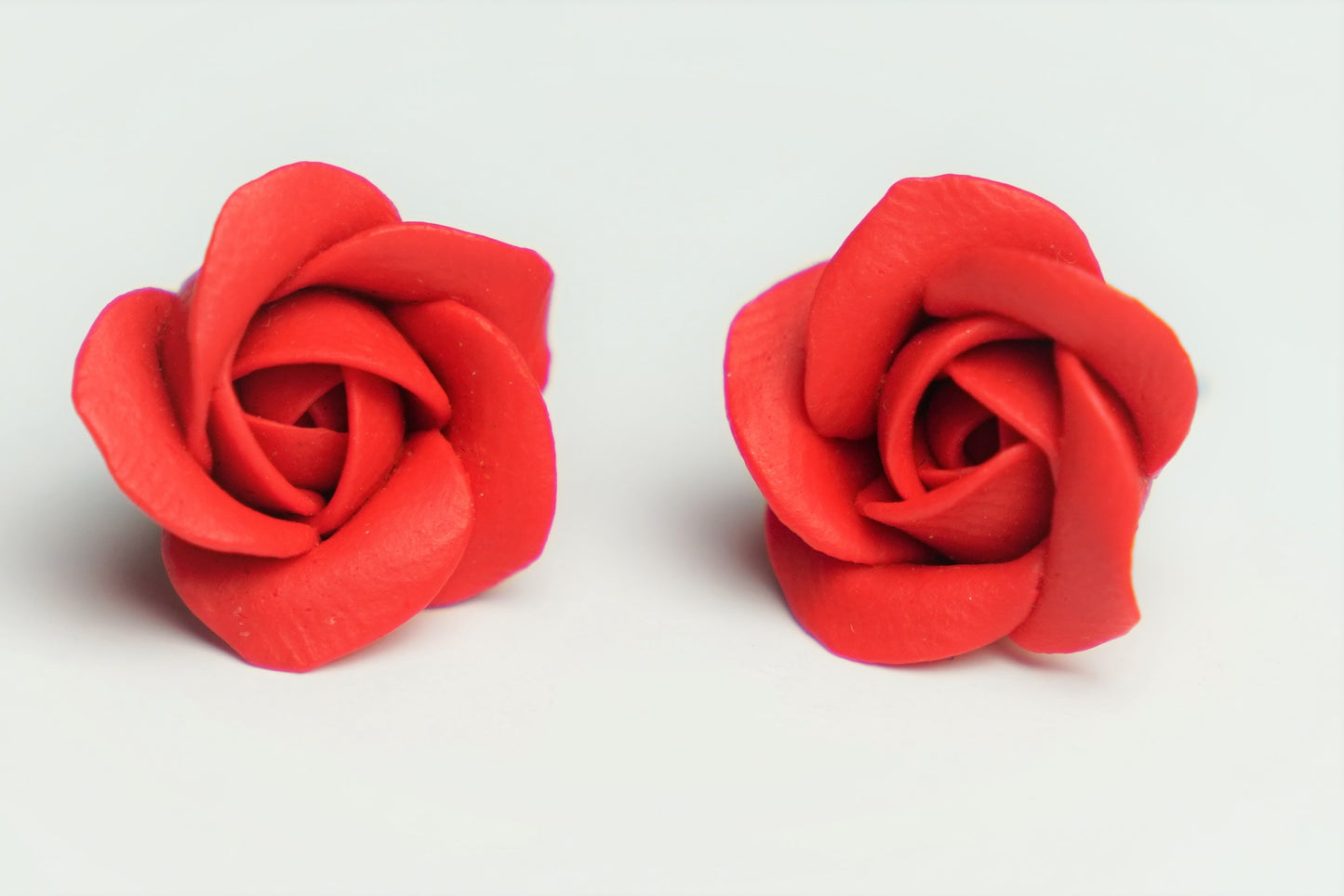 Pair of handmade polymer clay red rose stud earrings with sculpted petals, front view close-up