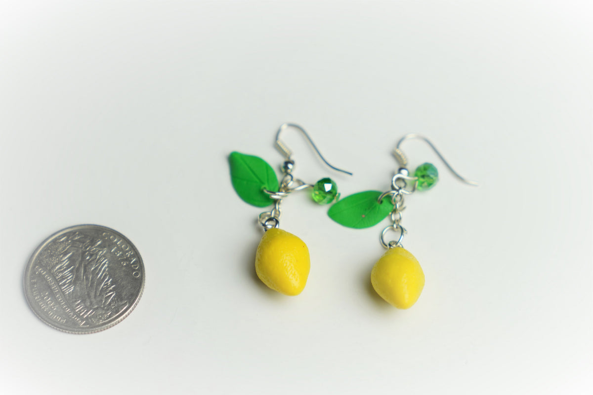 Lemon earrings in handmade polymer clay beside a quarter coin for size comparison on a white surface