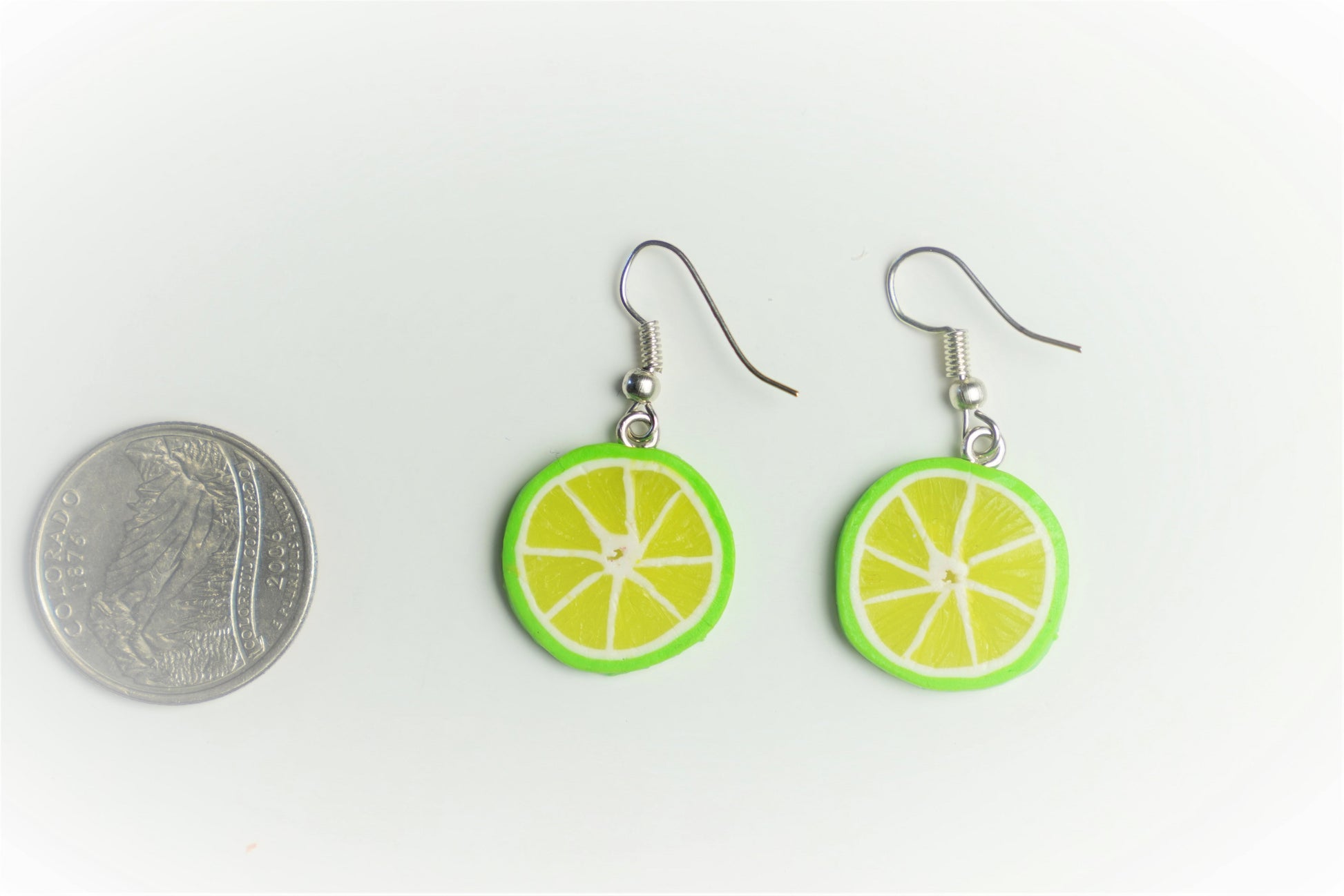 Lime slice earrings beside a quarter coin showing their size, flat lay on white