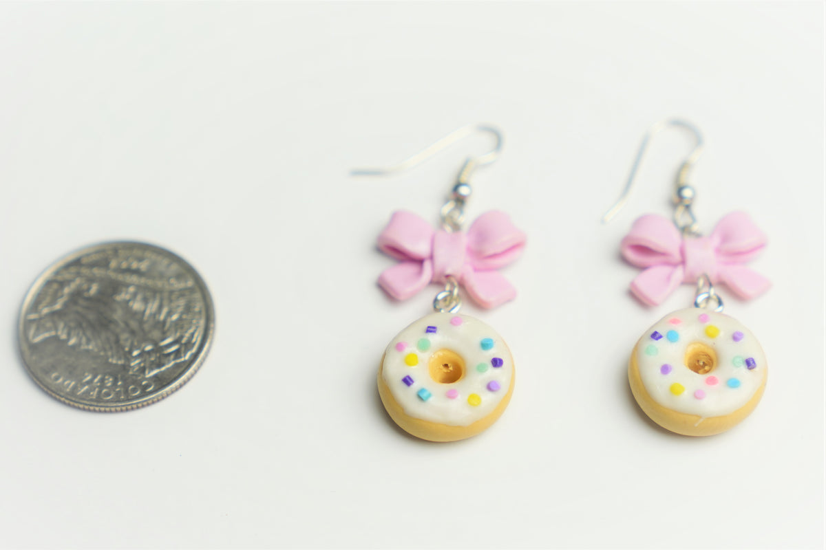 Polymer clay donut earrings beside a quarter coin for scale, white frosting with rainbow sprinkles