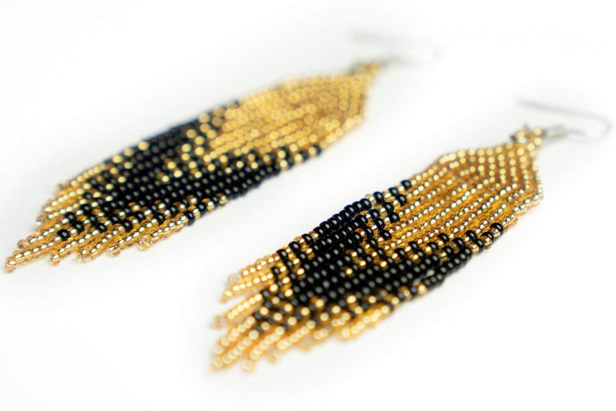 Detail of "Geometry Black&Gold" beaded earrings lying flat, showing woven gold tops and black fringe