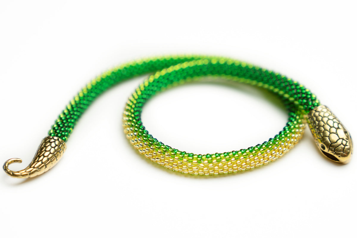 Green to yellow ombre crochet-beaded snake necklace coiled on white, brass snake head and hook tail