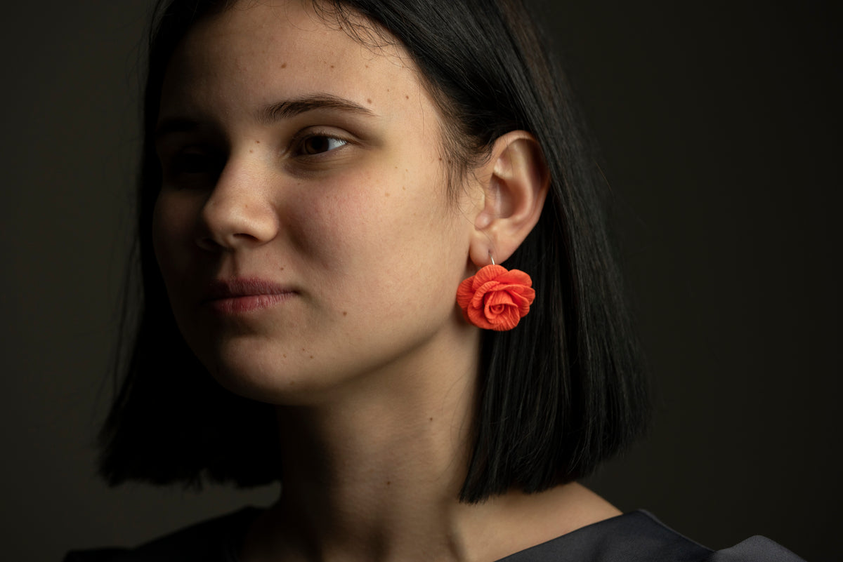 Model wearing a handmade polymer clay red rose earring, dark background portrait