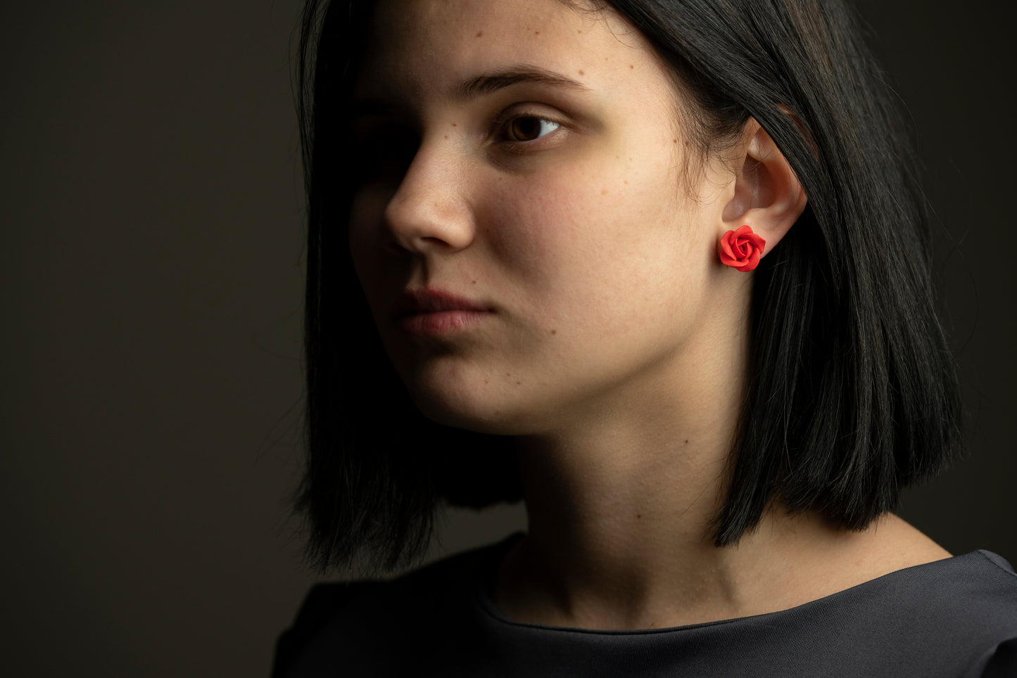 Model wearing a small red rose polymer clay stud earring, close-up profile view