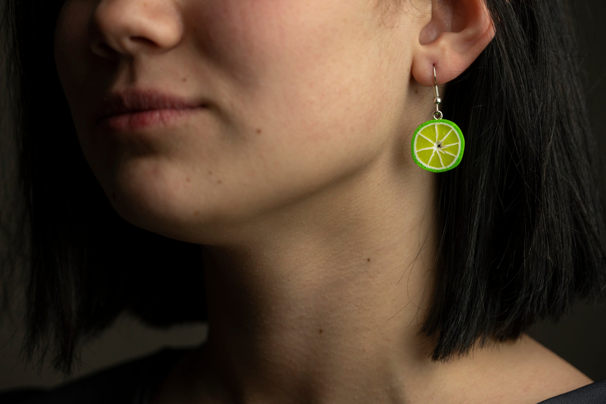 Model wearing a lime slice polymer clay earring, close-up of the ear and jawline