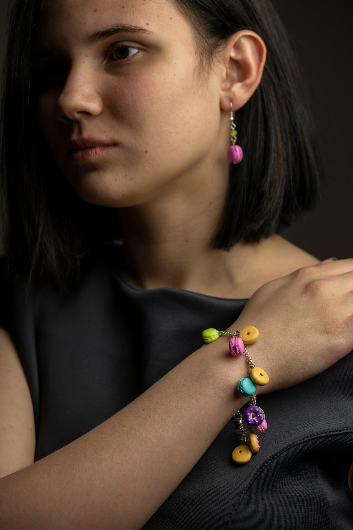 Model wearing the Donuts & Macarons bracelet with a matching pink macaron earring, dark portrait styling