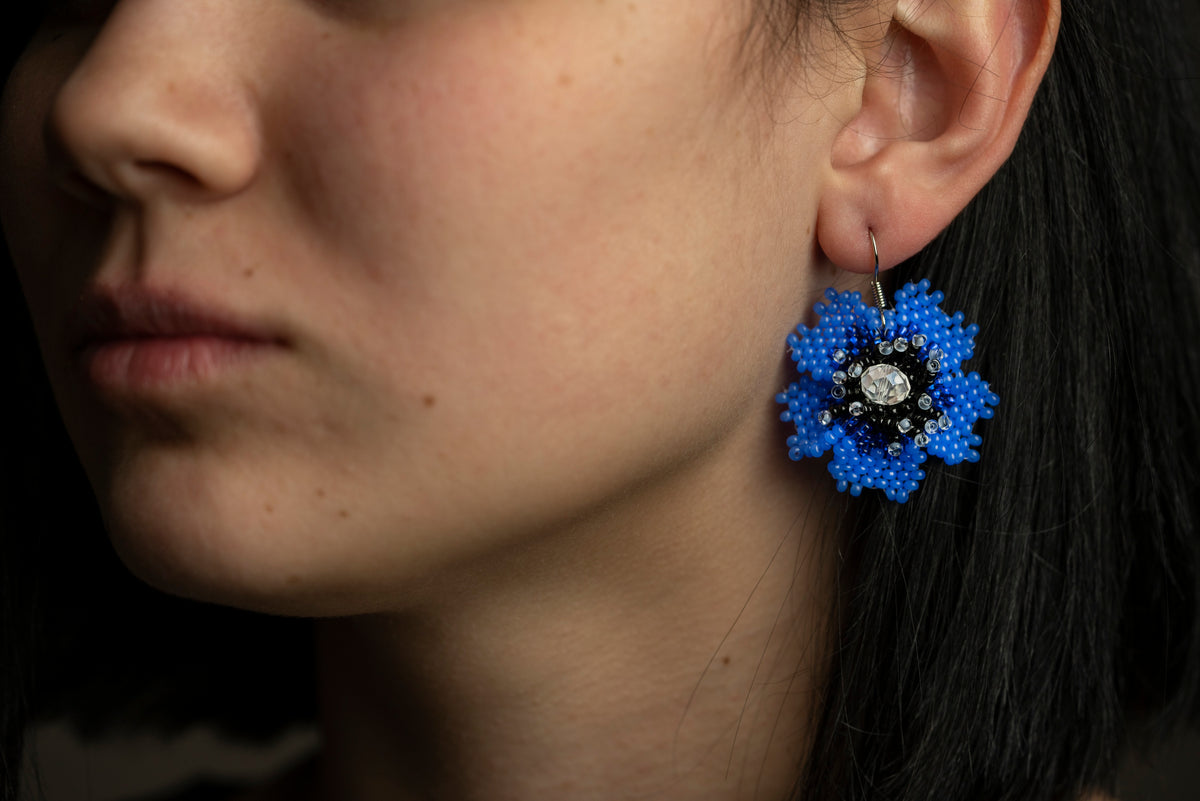Model wearing a blue beaded flower earring with a crystal center, close-up ear view