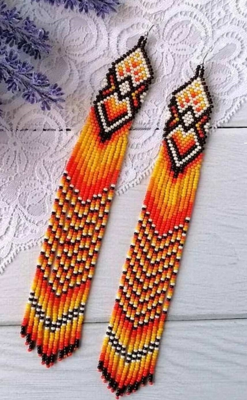 Extra long beaded earrings with orange, yellow and red fringe and brown tops, flat lay on white lace with lavender