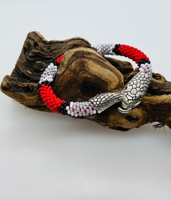 Beaded snake bracelet in red, white and gray glass seed beads with silver snake head clasp, draped on driftwood