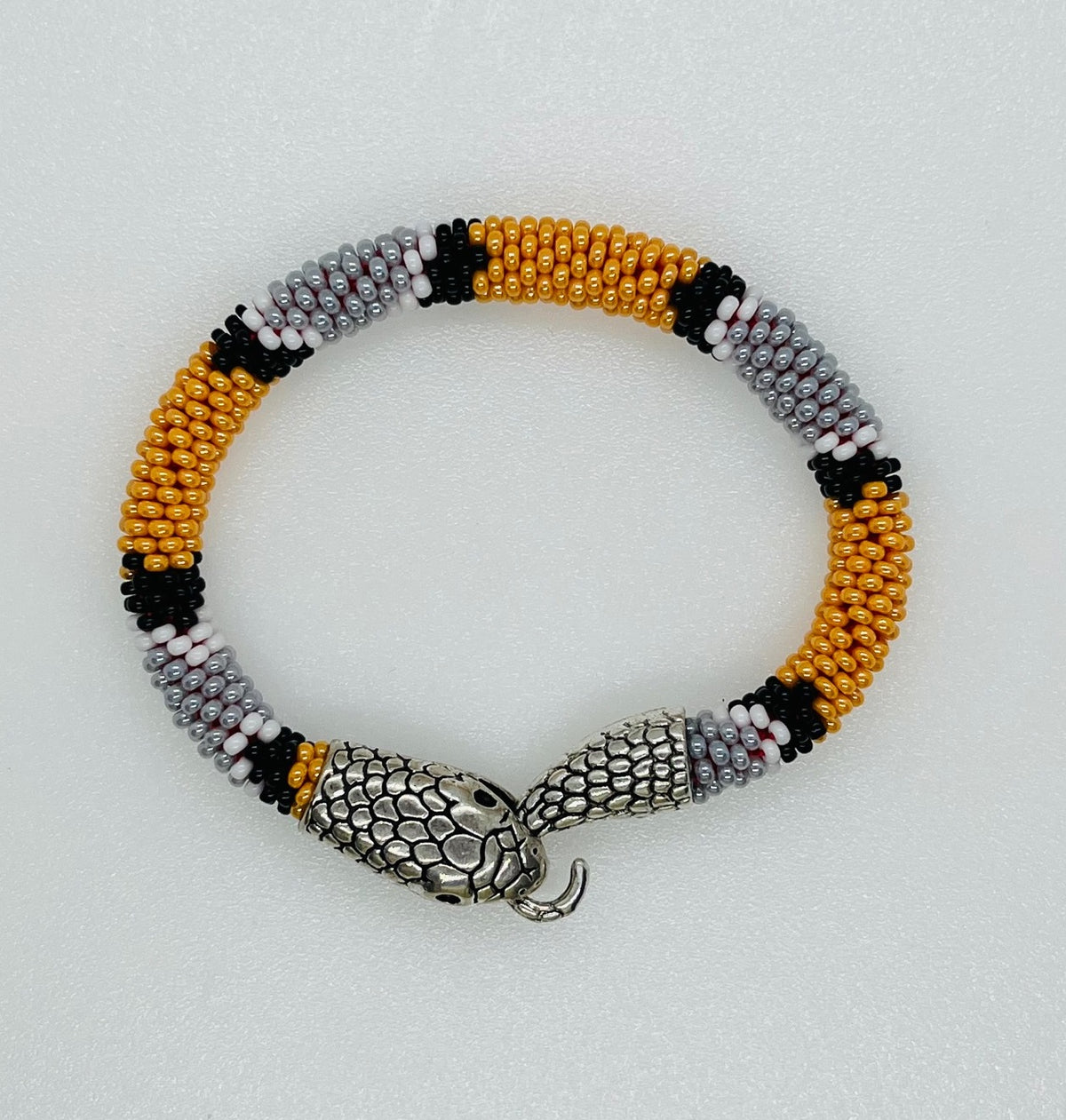 Handmade bead crochet snake bracelet in orange, gray and black stripes with silver snake head clasp, top view