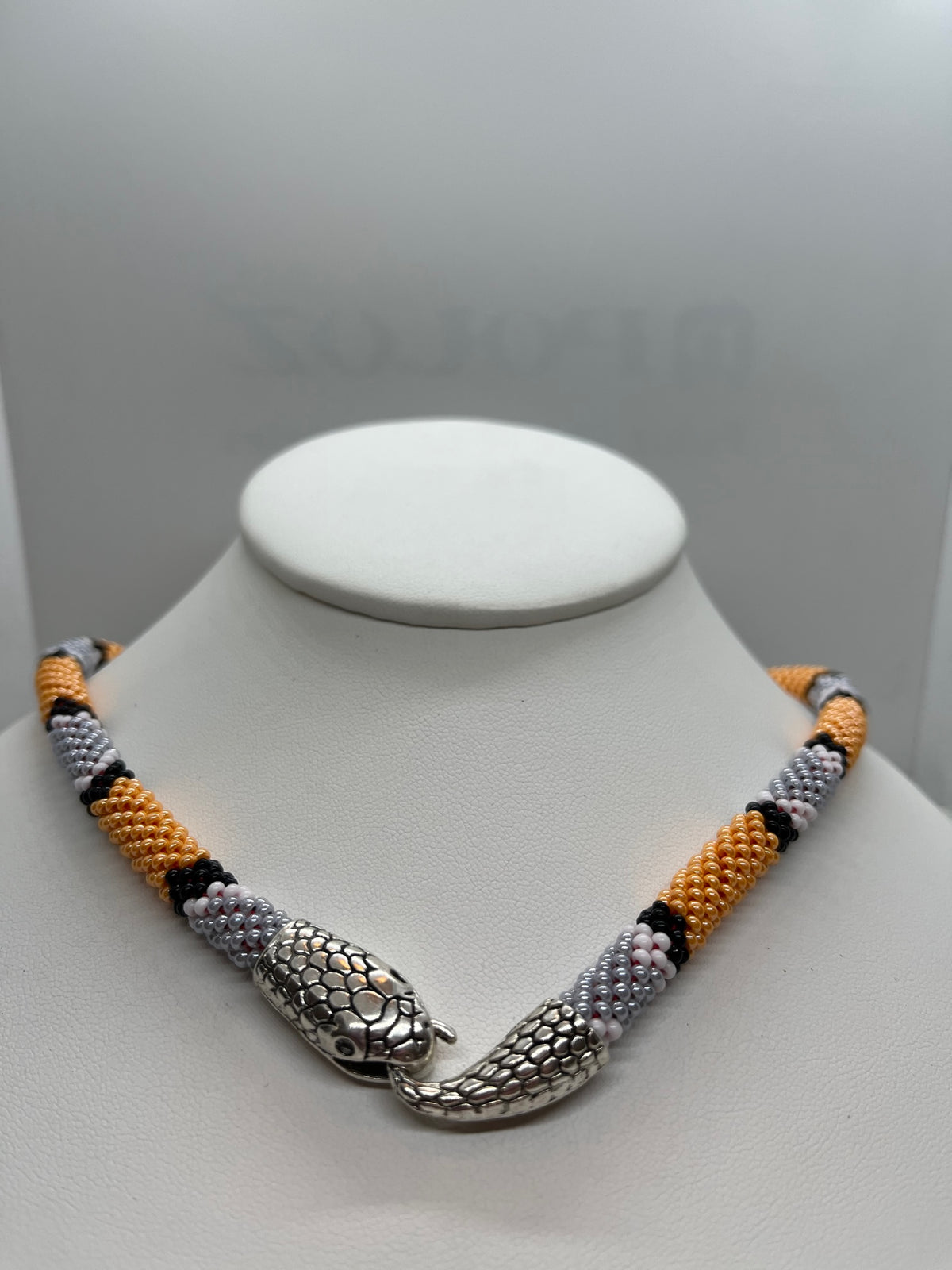 Orange and gray beaded snake choker on a white bust, close view of the silver snake head hook clasp