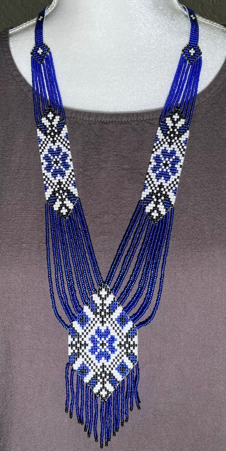 Cobalt blue gerdan necklace with white beaded flower ornament, Ukrainian folk style, on a draped mannequin