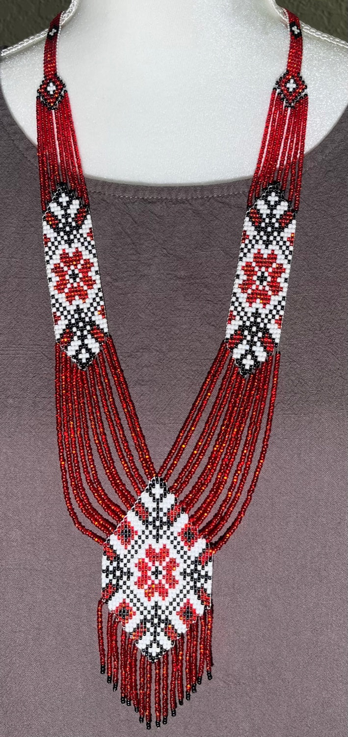 Red and white handmade gerdan necklace with folk flower motif and long beaded fringe on a gray-draped bust