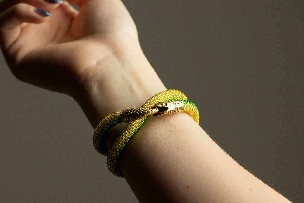 Yellow-green ombre beaded snake bracelet twisted twice around a model's wrist, gold snake head clasp