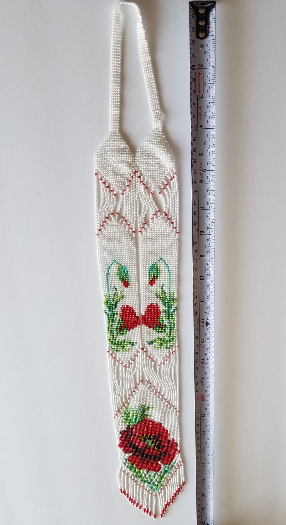 White loomed gerdan necklace with poppy pattern measured with a tape, flat lay on white