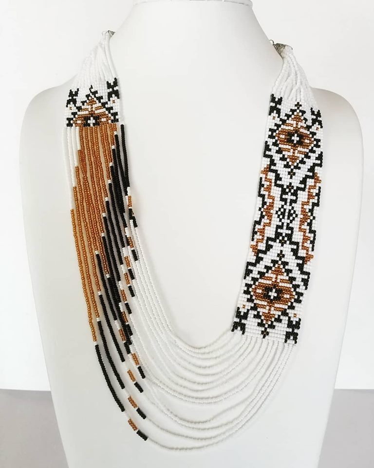 Asymmetric beaded necklace in white, copper and black with ornament panel on one side, on a display bust
