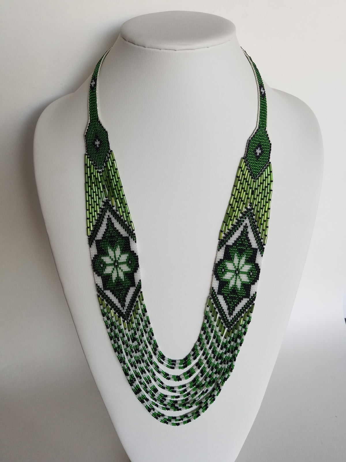 Handmade "Marichka" necklace crocheted from green and white glass seed beads, resting on a white display bust