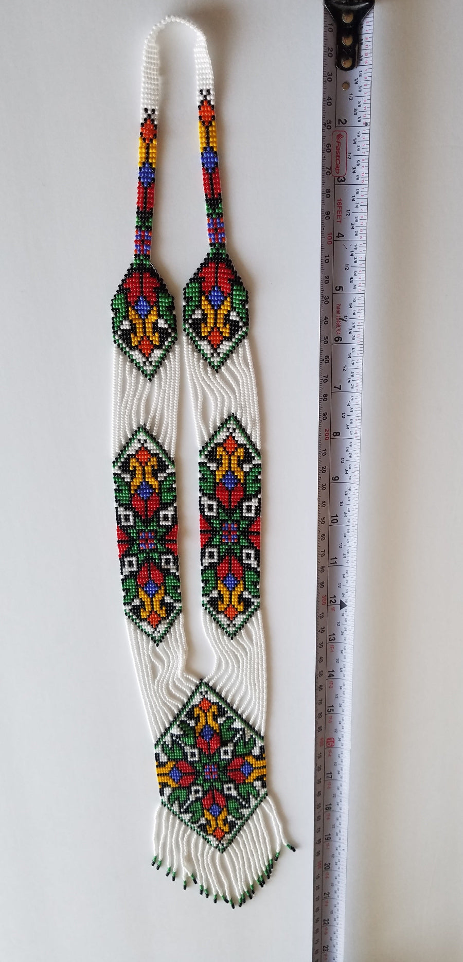 Loomed white gerdan necklace with traditional Ukrainian star pattern, flat lay beside a tape measure