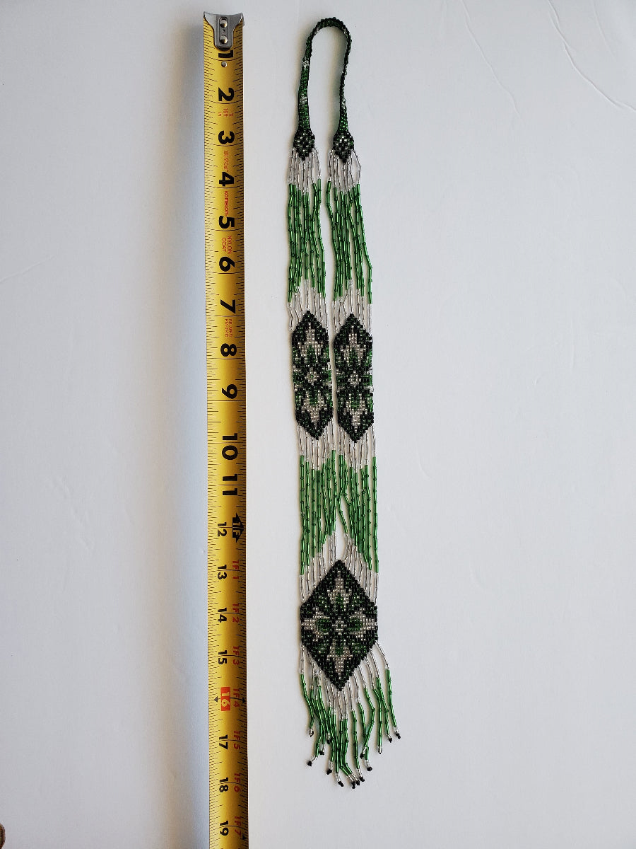 Green and white beaded gerdan necklace folded beside a tape measure to show sizing