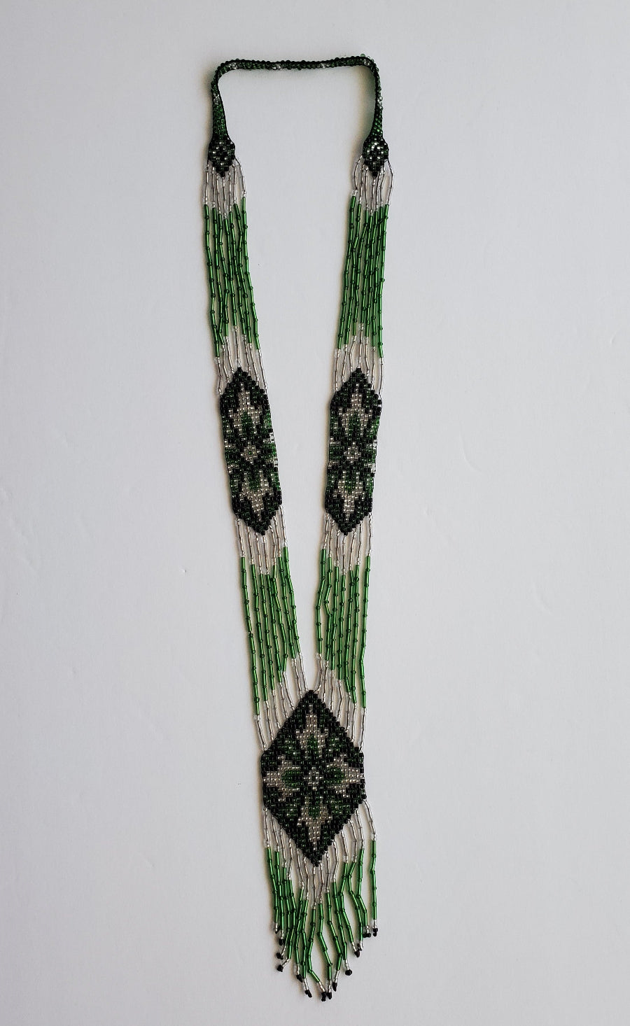 Green, white and black handmade gerdan necklace with floral diamond panels, flat lay on white
