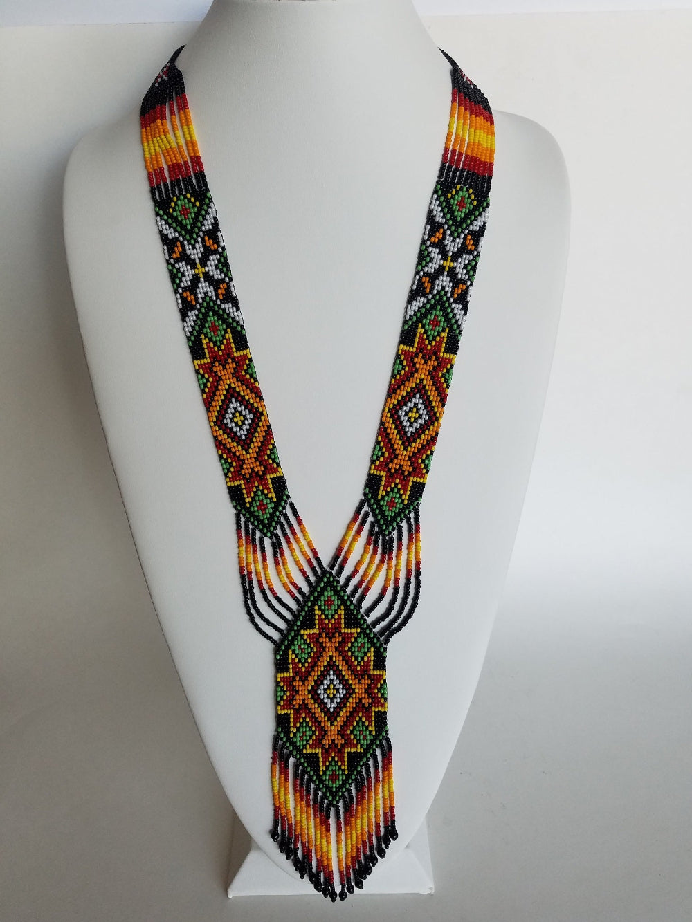 Handmade beaded gerdan necklace with black, orange, green and white star medallions on a white display bust